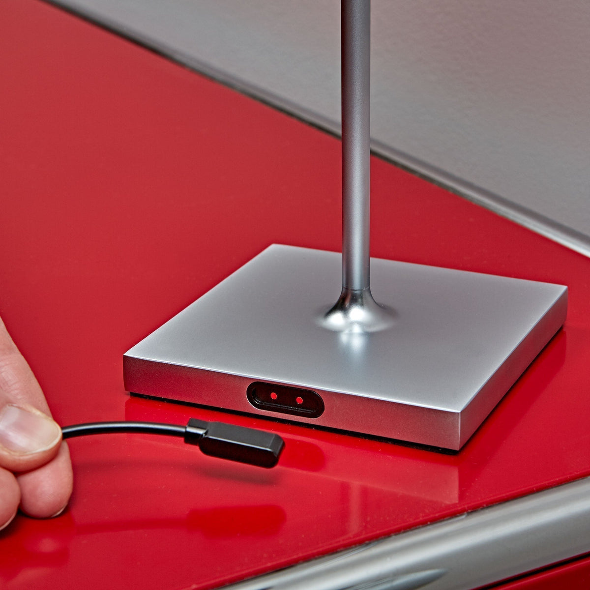 Magnetisches Easy-Connect-Ladekabel wird an den Lampenfuß einer Sigor Nuindie eckig in Silber angesetzt, die zwei Kontaktstifte im ovalen Anschluss sind sichtbar.