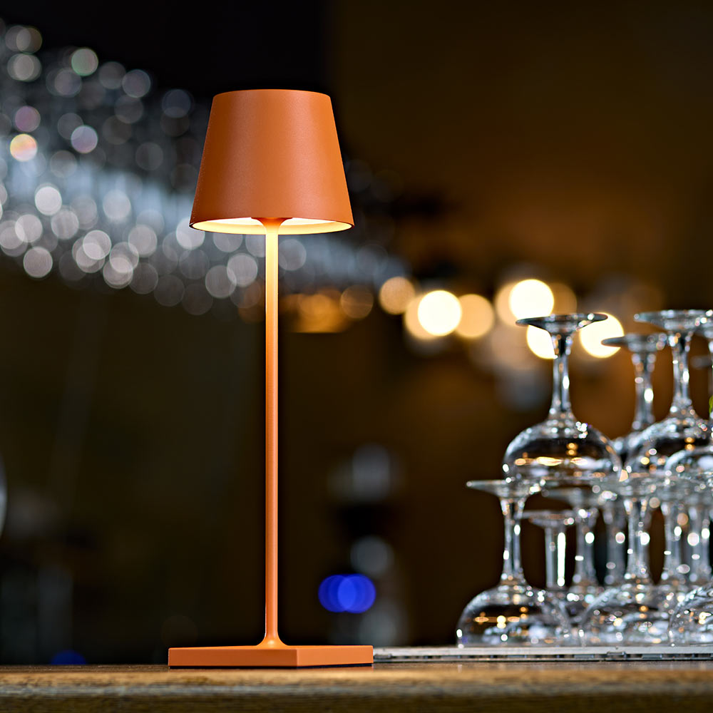 Eine Nuindie 3.0 Akku-Tischleuchte in orange auf einem Tresen in der Gastronomie