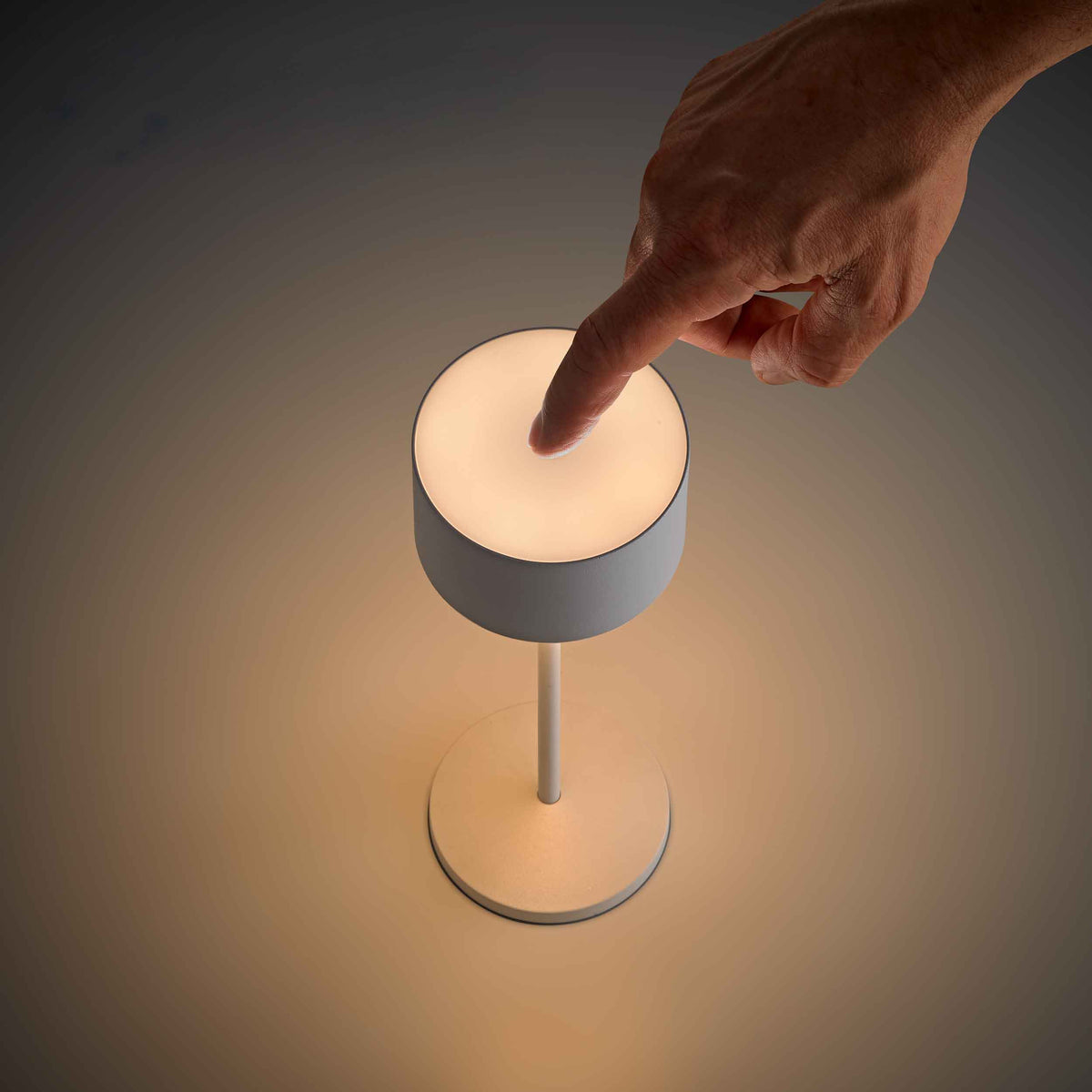 Hand bedient Sigor Veluna LED-Tischleuchte per Touch-Steuerung und dimmt das Licht stufenlos von Warmweiss zu Warmweiss extra im Gastronomiebetrieb